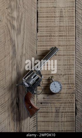 Wild west cowboys six gun, revolve, and pocket watch showing 12 noon, laying on old wooden boards. Stock Photo