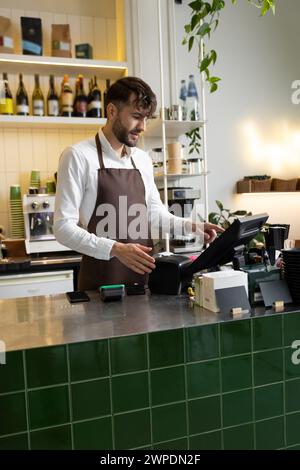 Man waiter working in coffee shop using terminal while standing at counter Stock Photo