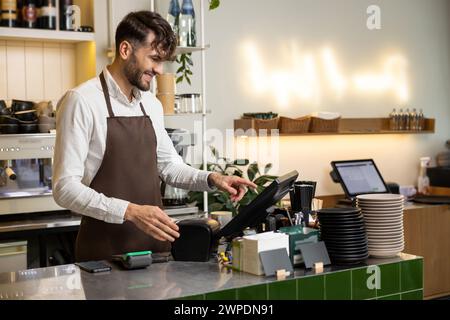 Man waiter working in coffee shop using terminal while standing at counter Stock Photo
