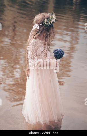 Nice young lady posing in pond water in apparel with lavender bouquet Stock Photo