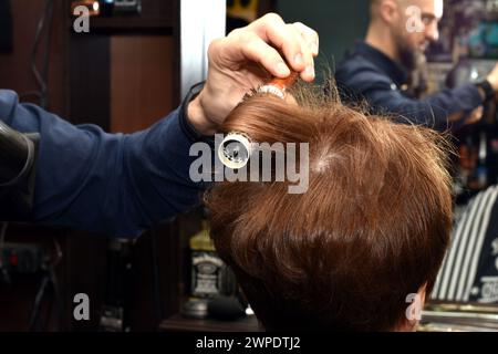 The hairdresser combs the hair on the client's head with a comb. Stock Photo