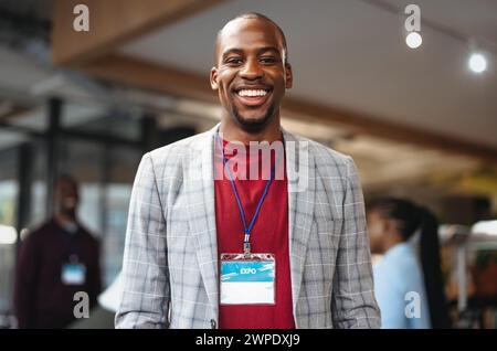 Happy young businessman wearing an ID badge at a professional expo. He smiles confidently, representing success, approachability, and positive corpora Stock Photo