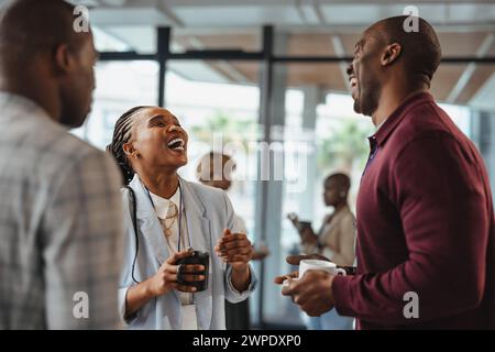 Three business professionals share a laugh during a coffee break at work. Group of colleagues having a funny conversation while standing together in a Stock Photo
