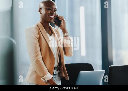 Successful businesswoman standing in her office, using her smartphone for communication. She appears happy and professional, discussing and speaking w Stock Photo