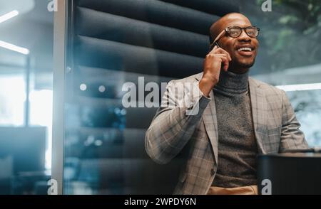 Businessman in an office space, using his smartphone to communicate and discuss business success. The entrepreneur wears glasses and appears happy and Stock Photo