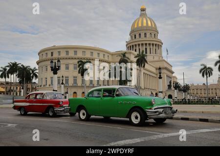 034 Red-white, green-white almendron cars -yank tank, Buick and Pontiac classics- from 1956-57 stop at a red light, Ntl.Capitol in back. Havana-Cuba. Stock Photo