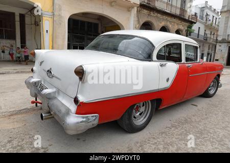 041 Oldtimer red-white almendron car -yank tank, Oldsmobile classic- from 1954 stops on the Plaza del Cristo Square. Old Havana-Cuba. Stock Photo