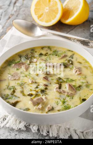 Greek Easter soup Magiritsa with lamb offal, herbs, seasoned with egg and lemon sauce close-up in a bowl on a marble table. Vertical Stock Photo