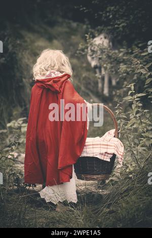 Little red riding hood with basket of food waiting for wolf in forest Stock Photo