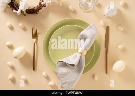 Easter table setting with green plates, bunny, painted eggs on beige background. View from above. Happy Easter celebration. Stock Photo