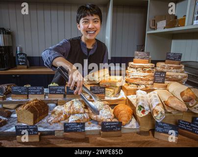 Young Asian woman smiling at bakery counter, serving an almond croissant in a modern cafe or restaurant Stock Photo