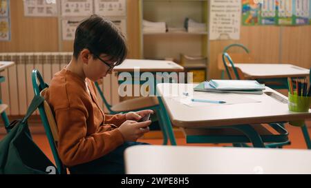 Child kid son pupil student bad behavior boy schoolboy playing video game on mobile phone at lesson at school hide smartphone under class desk Stock Photo