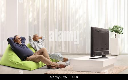 Mature man and a guy sitting on green bean bags in front of tv in an apartment Stock Photo