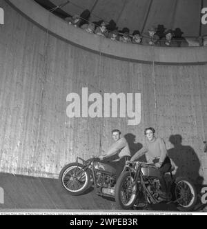 Wall of death 1949. The wall of death, motordrome, velodrome or well of death is a carnival sideshow featuring a silo- or barrel-shaped wooden cylinder, typically ranging from 20 to 36 feet (6.1 to 11.0 m) in diameter and made of wooden planks, inside which motorcyclists travel along the vertical wall and perform stunts, held in place by friction and centrifugal force. The original wall of death was in 1911 on Coney Island in the United States. Pictured a motorcyclist in high speed in the velodrome, showing off, with his hands in the air, not on the handlebars as he should. Sweden 1947. Conard Stock Photo