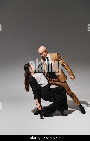 brunette young woman in suit and high heels performing dance with her partner on grey backdrop Stock Photo