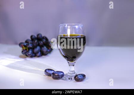 Glass of tasty dark wine and bunch of black grapes isolated on Blue background, side view Stock Photo
