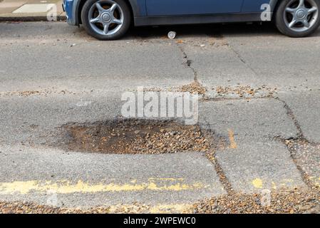 Large pothole in a road in Westcliff on Sea, Southend, Essex, UK, in need of repair. Parked car by pot hole. See image  2WPFXCG for repair Stock Photo