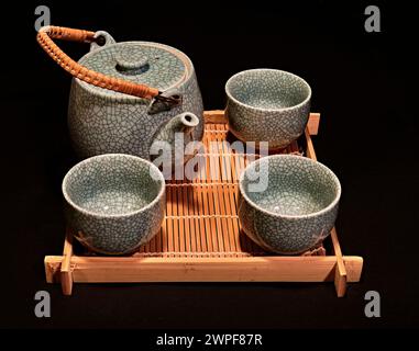 A still life of a ceramic ceremonial chinese,japanese tea set. On a bamboo tray,with a black background. Stock Photo