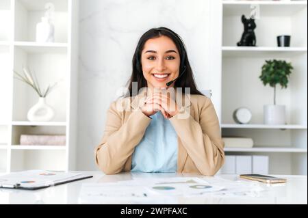 Online communication. Successful arabian or indian woman with headset, teacher, business consultant sits in the office during online consultation with client, smile, listening intercolar interlocutor Stock Photo