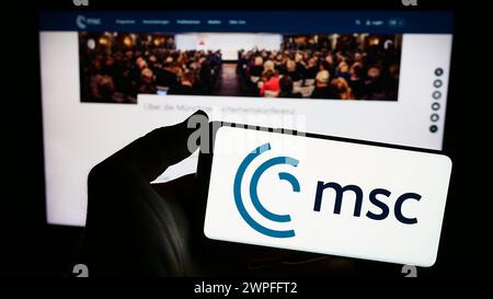 Person holding smartphone with logo of annual event Munich Security Conference (MSC) in front of website. Focus on phone display. Stock Photo