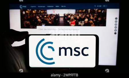 Person holding cellphone with logo of annual event Munich Security Conference (MSC) in front of webpage. Focus on phone display. Stock Photo