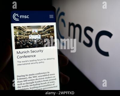Person holding smartphone with web page of annual event Munich Security Conference (MSC) in front of logo. Focus on center of phone display. Stock Photo