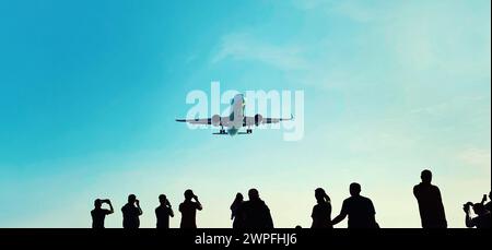 Silhouette of group of unknown people tourists take pictures a landing passenger airplane flying in blue sky background Stock Photo