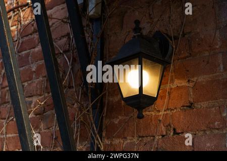 A bright light fixture mounted on the exterior wall of a building, casting light on the surrounding area at night. Stock Photo