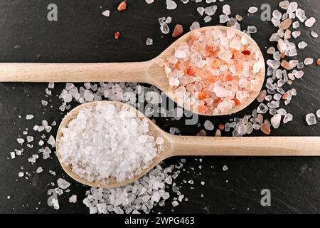 two different types of coarse salt on wooden cooking spoons on black slate background, top view of white sea salt and pink himalayan salt Stock Photo