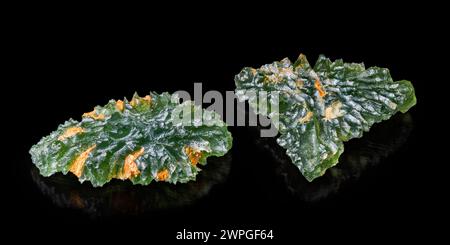 Rare tektite minerals moldavites with orange stains on green wrinkly surface. Raw uncut gemstones of meteoric glass and reflection on black background. Stock Photo