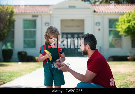 School boy going to school with father. Little schoolboy eating tasty lunch outdoors. School lunch for child. Stock Photo