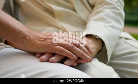Close up unrecognizable wrinkled hand elderly old senior aged man and woman married couple husband wife holding hands outside love support family Stock Photo