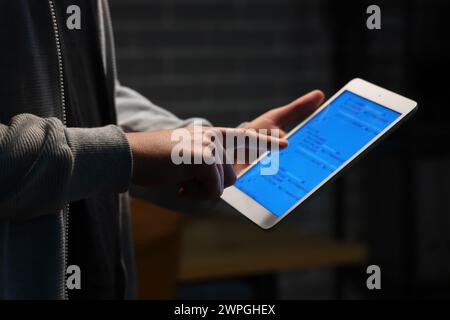 Hacker using tablet computer in dark room, closeup Stock Photo