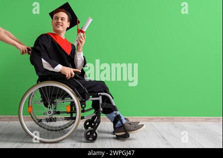 Male graduate in wheelchair with diploma near green wall Stock Photo