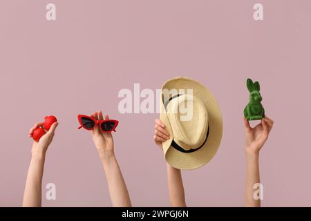 Female hands holding sunglasses with hat, toy bunny and Easter eggs on pink background. Holiday travel concept Stock Photo