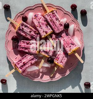 A platter of homemade cherry yogurt popsicles melting in bright sunlight. Stock Photo