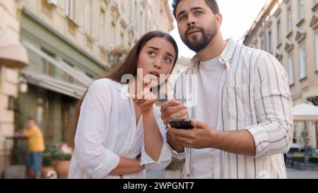 Couple Caucasian man woman using mobile phone smartphone internet maps location tourism trip tour GPS navigation app city center outside street Stock Photo