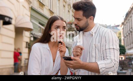 Couple Caucasian man woman using mobile phone smartphone internet maps location tourism trip tour GPS navigation app city center outside street Stock Photo