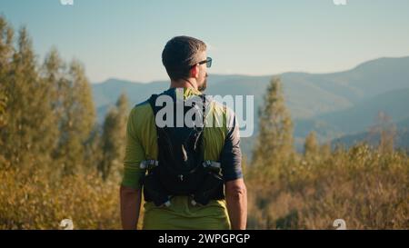 Back view thoughtful calm adult Caucasian male man guy sportsman mountaineer athlete rest hiking looking around enjoy atmosphere sport healthy Stock Photo