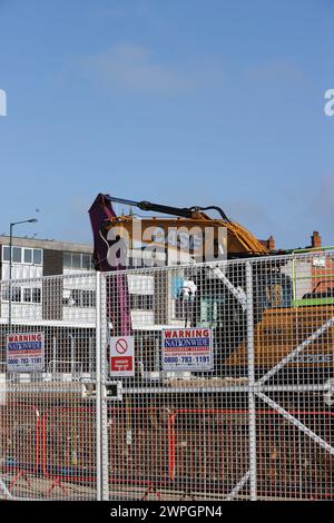 Tracked excavator behind fence with warning signs on construction site, radcliffe regeneration scheme, near bury, greater manchester uk Stock Photo