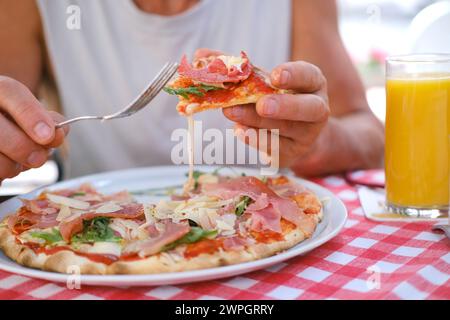 man eats Italian pizza, with salami, cheese, arugula, , male hands take pieces of pizza with salami, cheese, arugula, hands with food close-up, concep Stock Photo