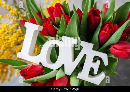 tulips with mimosa and the inscription love. Spring bouquet with mimosa flowers and red tulips - spring concept, spring natural background. Close-up Stock Photo