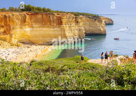 Tourists standing in the cliff to view the beautiful beach of Benagil in Algarve. Praia de Benagil beach, Algarve, Portugal, Europe. Stock Photo