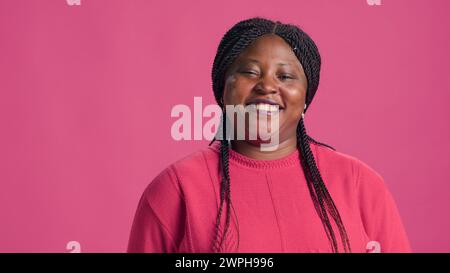 Video showcasing stylish african american woman with penchant for pink sweater fashion confidently striking poses. Genuine laughter of young lady infuses authentic charm to the close-up shot. Stock Photo