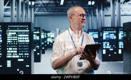 Happy computer scientist expertly managing data while navigating through industrial blade servers. Cheerful system administrator ensuring flawless cybersecurity defence, optimizing systems Stock Photo