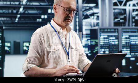 Trained engineer expertly managing data while navigating in industrial server room. Specialist ensuring errorless cybersecurity protection, optimizing systems and performing necessary updates Stock Photo