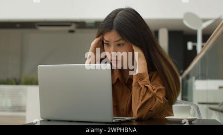 Exhausted overworked Asian chinese japanese woman student girl studying online with laptop in cafe tired sick businesswoman think difficult decision Stock Photo