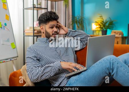 Frustrated Indian man having software problems with laptop angry guy nervous seeing error or mistake notification at computer screen mad employee experience virus attack or app malfunction. Lifestyles Stock Photo