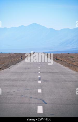 Empty asphalt straight highway road in Mongolia between mongolian towns Khovd and Altai under blue sky. Bumbat Khairkhan Ridge on background. Stock Photo