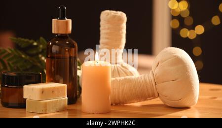 Spa composition. Cosmetic products, herbal bags and burning candle on wooden table, closeup Stock Photo